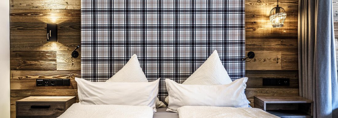 A modern bedroom with a cozy double bed and a checkered headboard. The wooden paneling and warm lights create an inviting atmosphere. - The Peak Sölden - Sölden