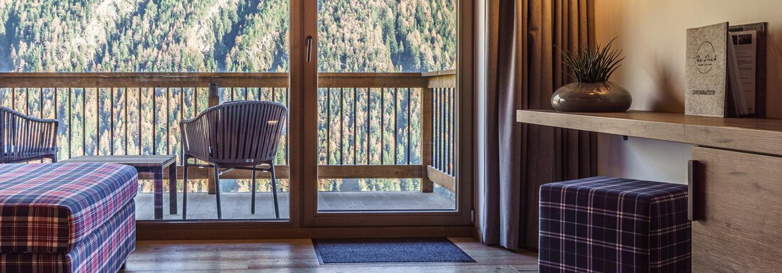 A cozy room with wooden floors and large windows offering a view of the mountains. There is seating and a decorative table in the interior. - The Peak Sölden - Sölden