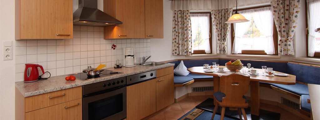 A modern kitchen with wooden cabinets, a stove, and a cozy dining area. Large windows provide plenty of light and an inviting atmosphere. - Toni's Ferienheim - Sölden