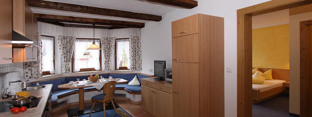 A cozy kitchen with wooden shelves and a dining area. The room has large windows and is decorated in a friendly and bright manner. - Toni's Ferienheim - Sölden