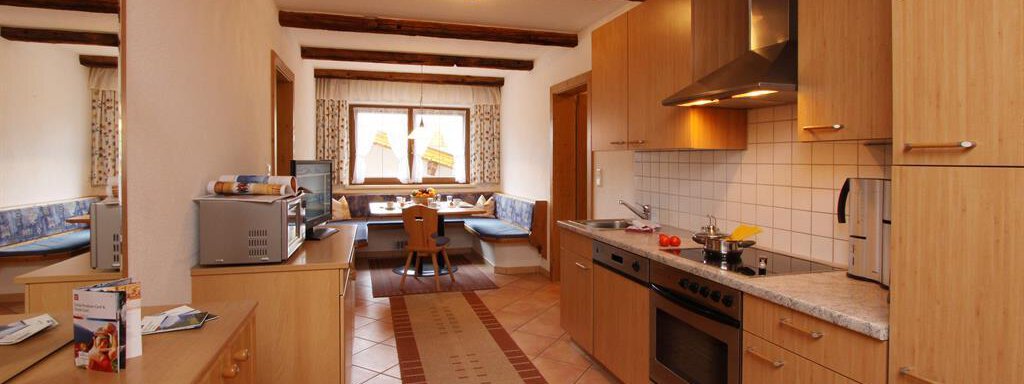 A modern kitchen with wooden cabinets and high-quality appliances. In the background, there is a cozy dining area with a table and chairs. - Toni's Ferienheim - Sölden