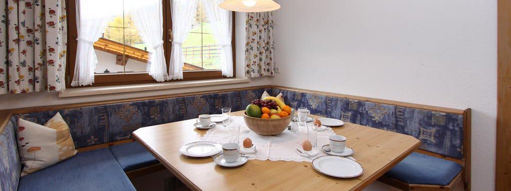 A cozy dining area with a wooden table and a blue bench. The table is set with dishes and a fruit bowl. - Toni's Ferienheim - Sölden