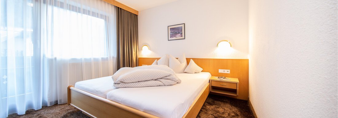 A modern bedroom with a large double bed and soft carpet flooring. Large windows allow plenty of light in and create an inviting atmosphere. - Toni's Ferienheim - Sölden