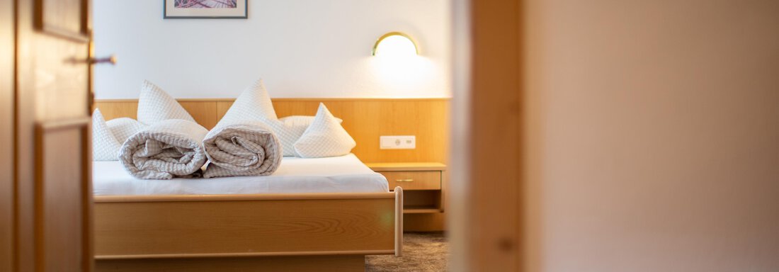 A cozy bedroom with a large bed and two pillows. The room has a warm atmosphere with soft light and a picture on the wall. - Toni's Ferienheim - Sölden