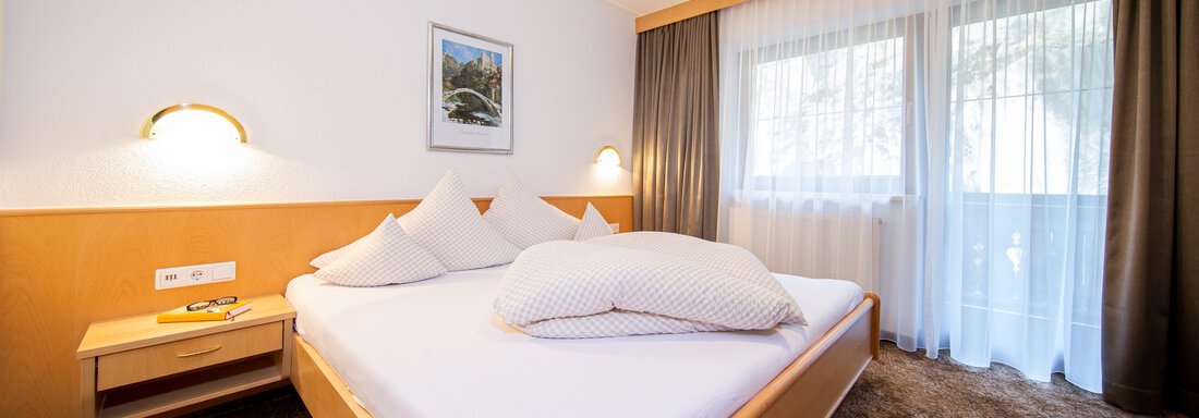 A modern bedroom with a large bed and soft pillows. Windows with curtains let in plenty of daylight. - Toni's Ferienheim - Sölden