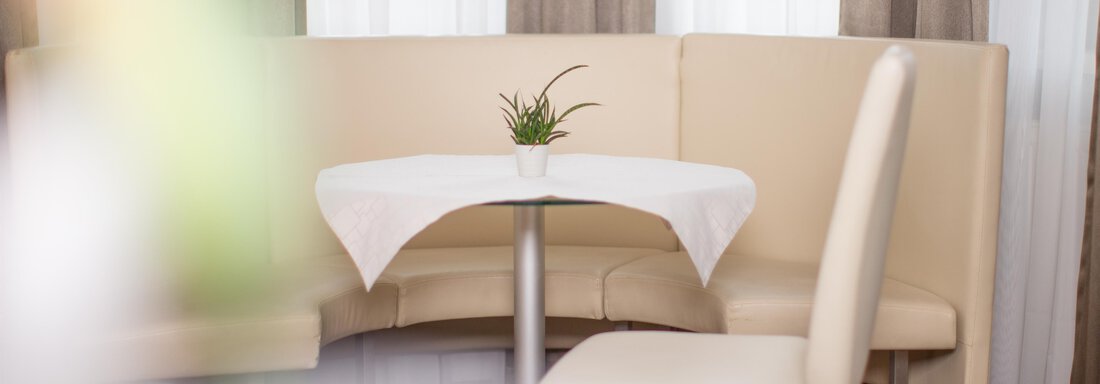 A small table in a cozy restaurant with bright, upholstered seats. On the table sits a small pot with a plant. - Toni's Ferienheim - Sölden