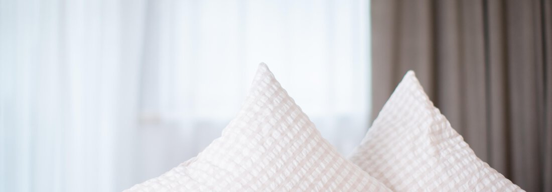 Two elegant, white pillows are lying on a bed. In the background, bright curtains can be seen. - Toni's Ferienheim - Sölden