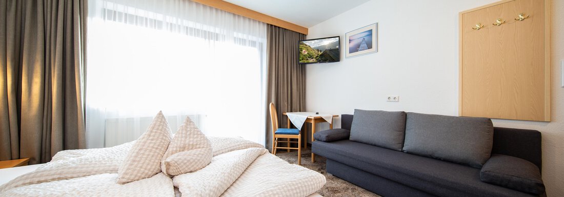 App2 Zimmer A cozy room with a double bed and a sofa bed. The room has large windows that let in plenty of natural light. - Toni's Ferienheim - Sölden