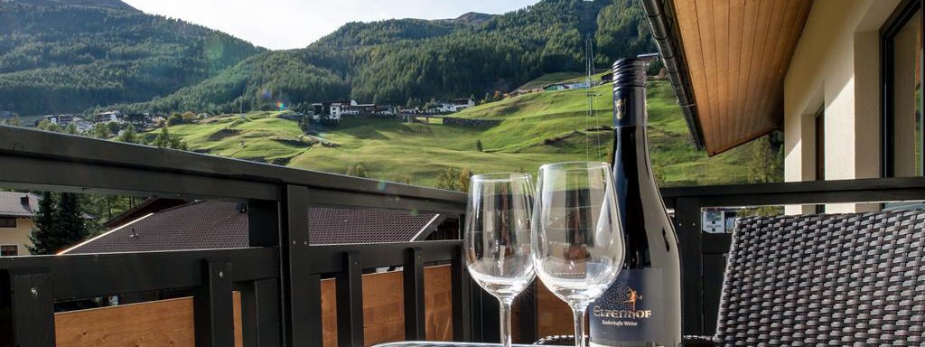 A balcony with a breathtaking view of the mountains. On the table are two glasses and a bottle of wine. - Top Apart Daniela - Sölden