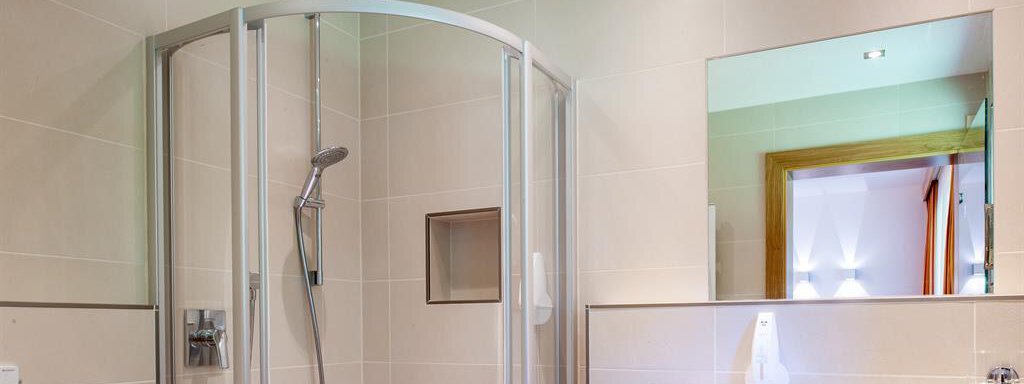 A modern bathroom with a shower cubicle and a sink. The walls are light and clean, and there is a large mirror wall. - Top Apart Daniela - Sölden