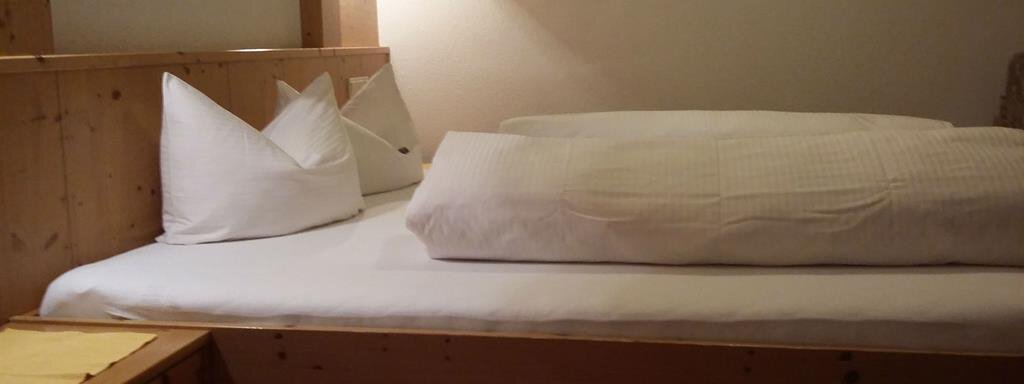 A cozy room with a wooden bed and white pillows. The warm lighting creates an inviting atmosphere. - Top Apart Daniela - Sölden