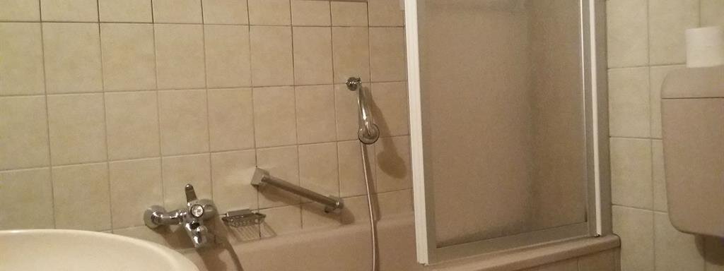 A simple bathroom with a bathtub, a shower cabin, and a sink. The walls are tiled with light tiles. - Top Apart Daniela - Sölden