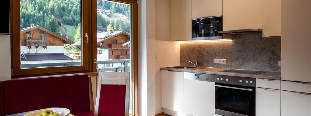 Küche Giggijoch A modern kitchen with bright furniture and large windows that provide a view of the mountains. The dining area is furnished with a table and red chairs. - Top Apart Daniela - Sölden