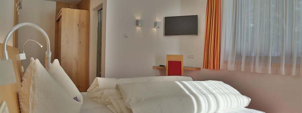 A cozy hotel room with a large bed and modern furniture. The walls are light and the room has a window with plenty of daylight. - Top Apart Daniela - Sölden