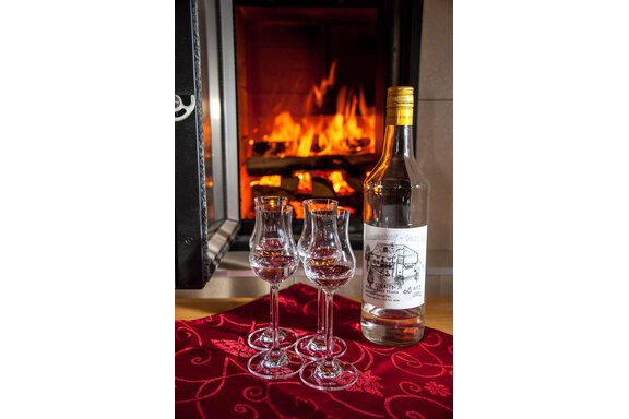 A bottle of schnapps stands next to three glasses on a table in front of a fireplace. The flames create a cozy atmosphere. - Top Apart Daniela - Sölden