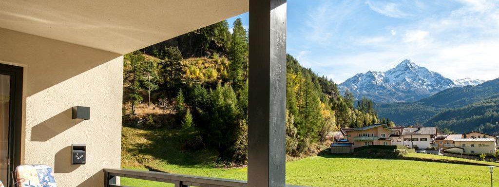A cozy balcony with a table and a chair. In the background, a picturesque mountain landscape stretches out with snow-capped peaks and green meadows. - Top Apart Daniela - Sölden