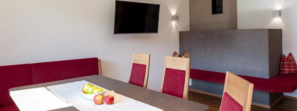 Panorama Apart mit Essbereich A modern dining room with a large table and red seat cushions. On the wall, there is a TV and a minimalist fireplace. - Top Apart Daniela - Sölden