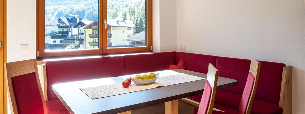 A bright dining room with a large table and red benches. Through the window, you can see a mountainous landscape. - Top Apart Daniela - Sölden