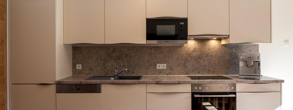 A modern kitchen with bright cabinets and a gray countertop. It is equipped with an oven, a stove, and a microwave. - Top Apart Daniela - Sölden