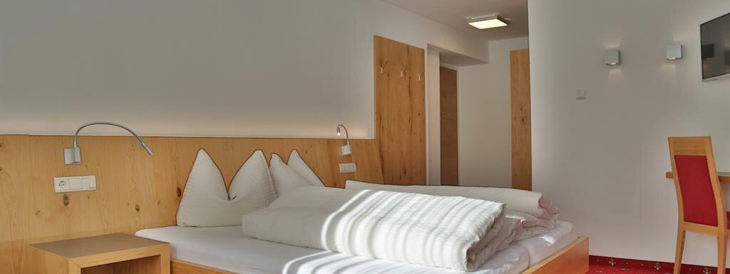 A cozy hotel room with wooden furniture and a red carpet. There is a large bed, a table, and a bright, inviting atmosphere. - Top Apart Daniela - Sölden