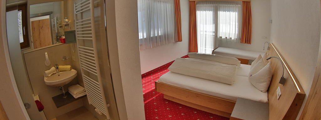 A comfortable room with a bathroom, a large window, and a cozy bed. The floor is red with a simple, modern design. - Top Apart Daniela - Sölden