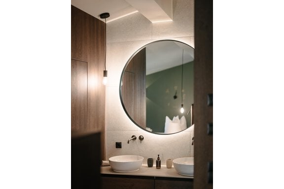 A modern bathroom with a large round mirror and two sinks. The walls are in warm wood and gray tones. - VIBES Sölden - your alpine homebase - Sölden