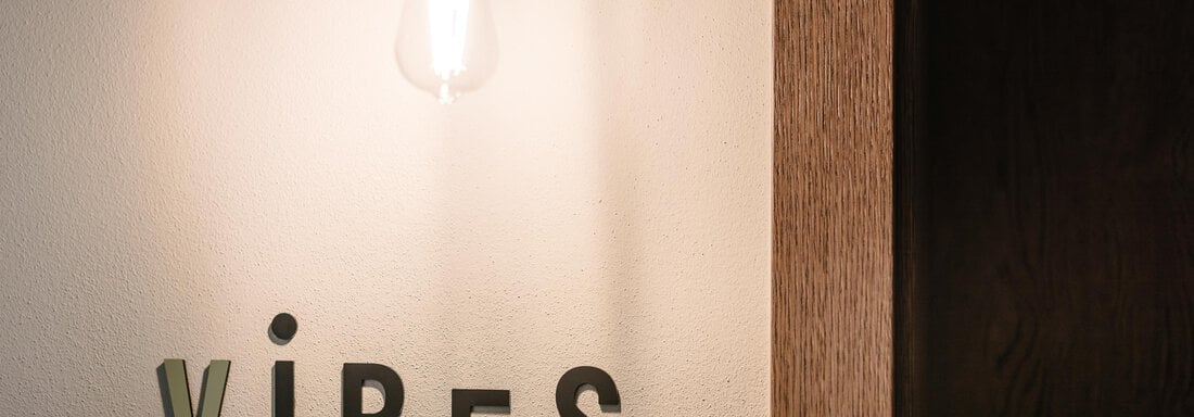 A wall area with warm light and the word "VIBES" in different fonts. The combination of wood and minimalist design creates an inviting atmosphere. - VIBES Sölden - your alpine homebase - Sölden
