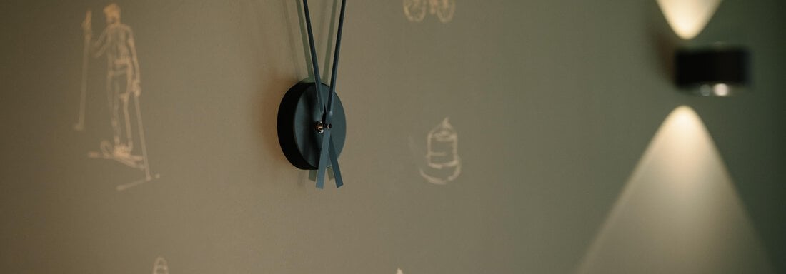 A wall clock with a modern design hangs on a green wall. Around the clock, bright drawings of various motifs can be seen. - VIBES Sölden - your alpine homebase - Sölden