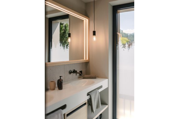 A modern bathroom with a large mirror and ambient lighting. The windows offer a view of the surroundings with trees. - VIBES Sölden - your alpine homebase - Sölden