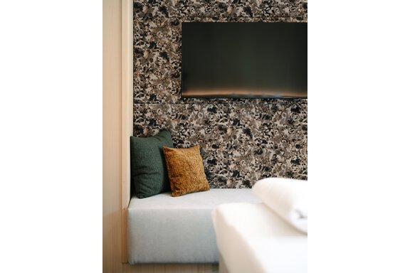 A modern room with a cozy bench and decorative cushions. On the wall, there is a television and an appealing wallpaper. - VIBES Sölden - your alpine homebase - Sölden