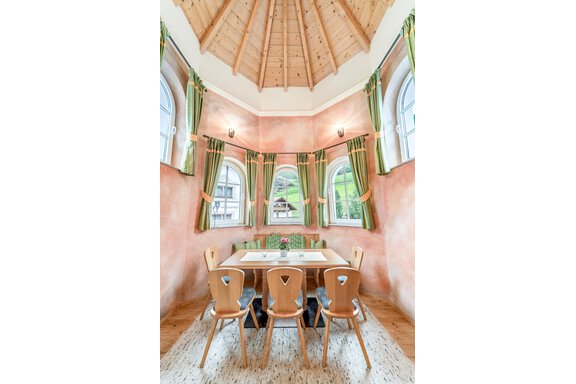 An inviting dining area with a round table and wooden chairs. Large windows with green curtains provide a beautiful view of the surroundings. - Villa Castelbell - Sölden