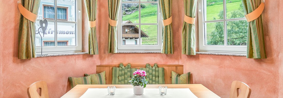A cozy dining area with a wooden table and comfortable chairs. Large windows provide a view of the green landscape outside. - Villa Castelbell - Sölden