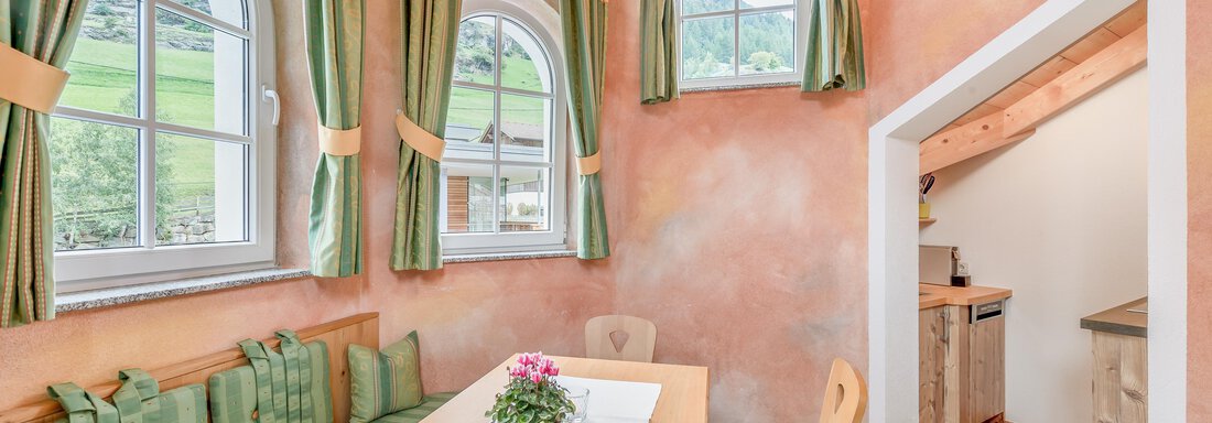 A cozy dining area with a long tabletop and benches. The walls are painted in soft colors and large windows provide plenty of light. - Villa Castelbell - Sölden