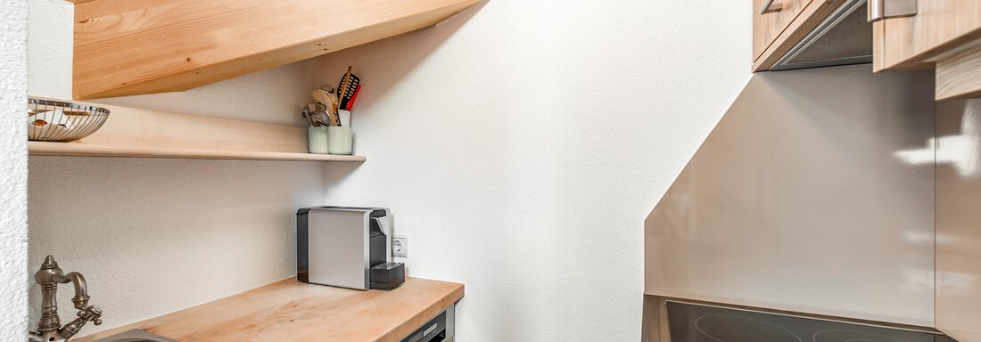 A modern kitchen with wooden shelves and a sloped roof. The equipment includes a sink, a stove, and a small kitchenette. - Villa Castelbell - Sölden