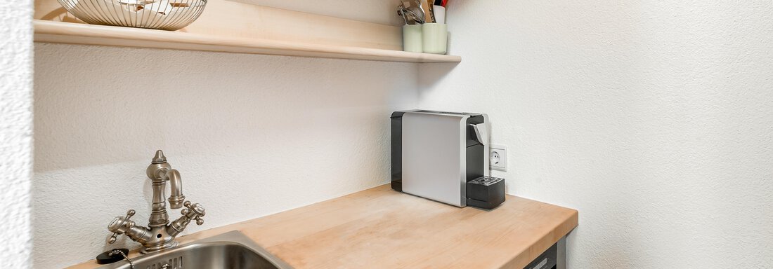 A small kitchenette with sink, wooden shelves, and a microwave. The room feels bright and modern. - Villa Castelbell - Sölden