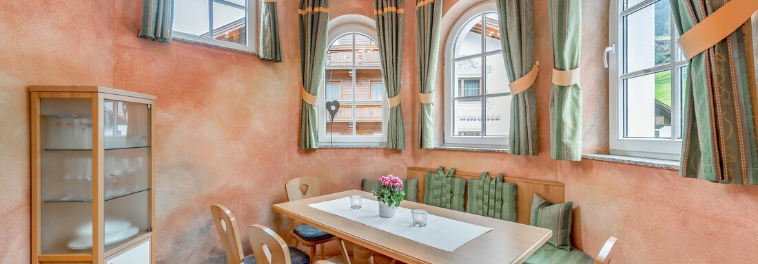 A cozy dining area with bright table decor. The walls are in warm color tones and large windows provide plenty of light. - Villa Castelbell - Sölden