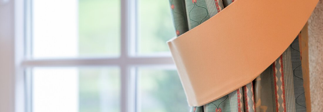 A part of a curtain with a decorative band is visible. In the background, there is a window with a view of a green landscape. - Villa Castelbell - Sölden