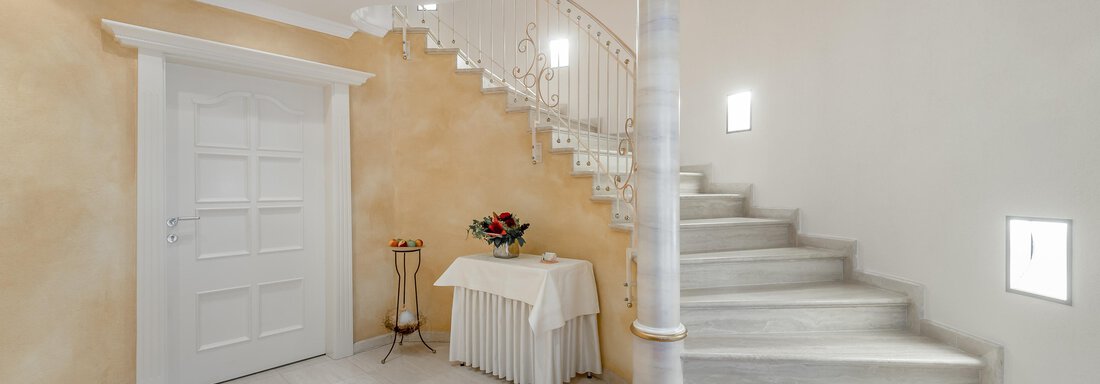 An elegant entrance area with a curving staircase. The walls are in warm colors, and there is a small table decoration. - Villa Castelbell - Sölden