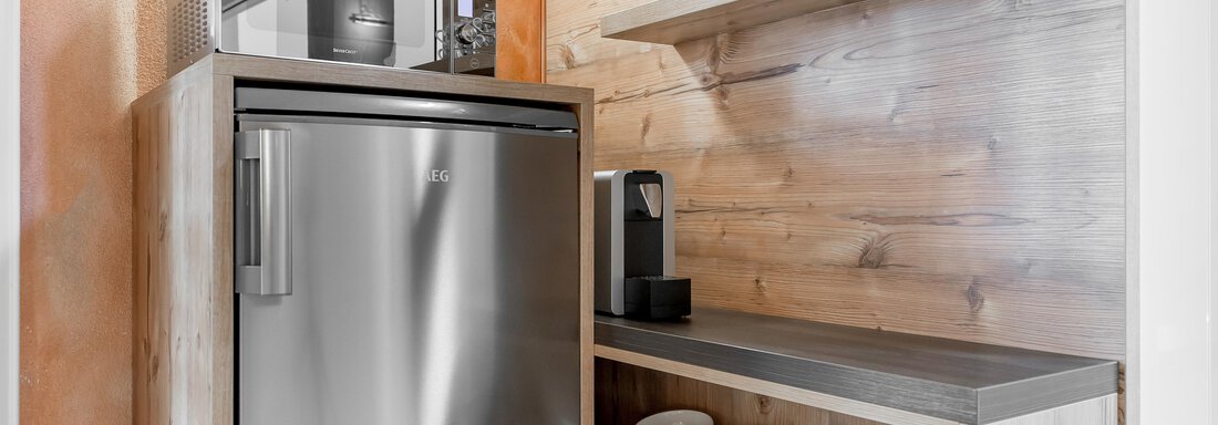 A modern kitchen unit with a stainless steel refrigerator and a microwave. On the shelves, cups and dishes are neatly arranged. - Villa Castelbell - Sölden