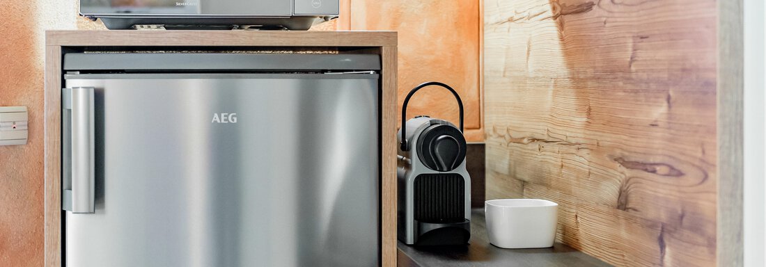 A modern kitchen with a refrigerator and a microwave. Next to the refrigerator stands a coffee capsule machine and a white bowl on the countertop. - Villa Castelbell - Sölden