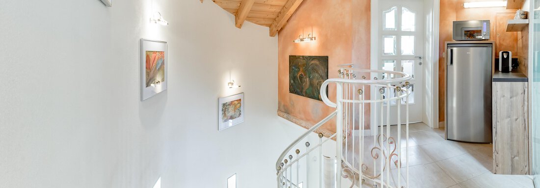 A bright staircase with an elegant railing leads into a modern room. The walls are in warm tones and there are some pictures for decoration. - Villa Castelbell - Sölden