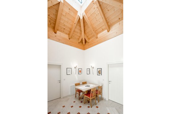 A bright room with wooden paneling and slanted walls. A table with chairs stands in the middle, surrounded by white doors. - Villa Castelbell - Sölden