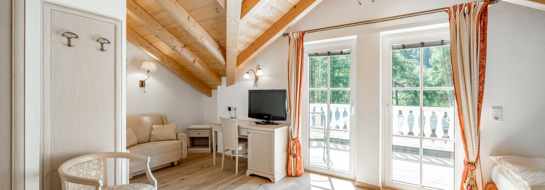 A bright and welcoming penthouse apartment with wooden ceilings. It features a living room, a television, and large windows overlooking nature. - Villa Castelbell - Sölden