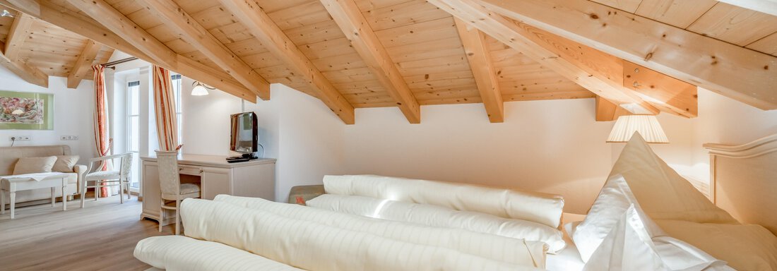 A cozy bedroom under a wooden roof with a large bed and many pillows. The decor is bright and inviting, ideal for relaxing. - Villa Castelbell - Sölden