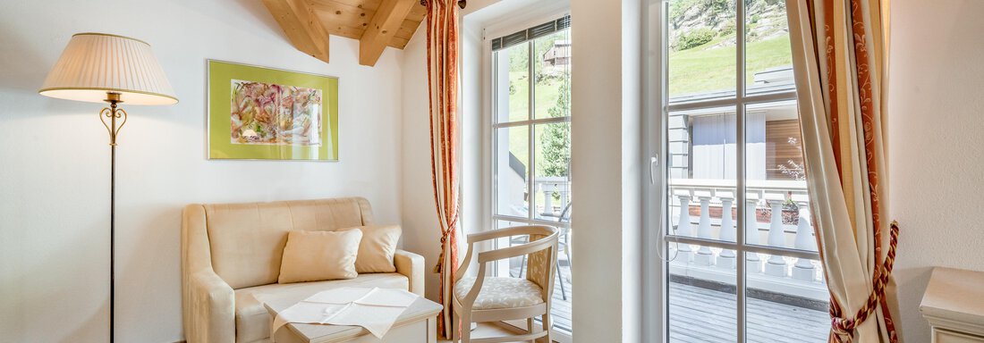 A bright living room with a wooden beam ceiling and modern furniture. Large windows offer a view of nature. - Villa Castelbell - Sölden