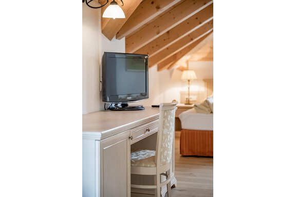 A cozy room with a desk and a television. The wooden beam ceiling and the orange bed create a warm atmosphere. - Villa Castelbell - Sölden