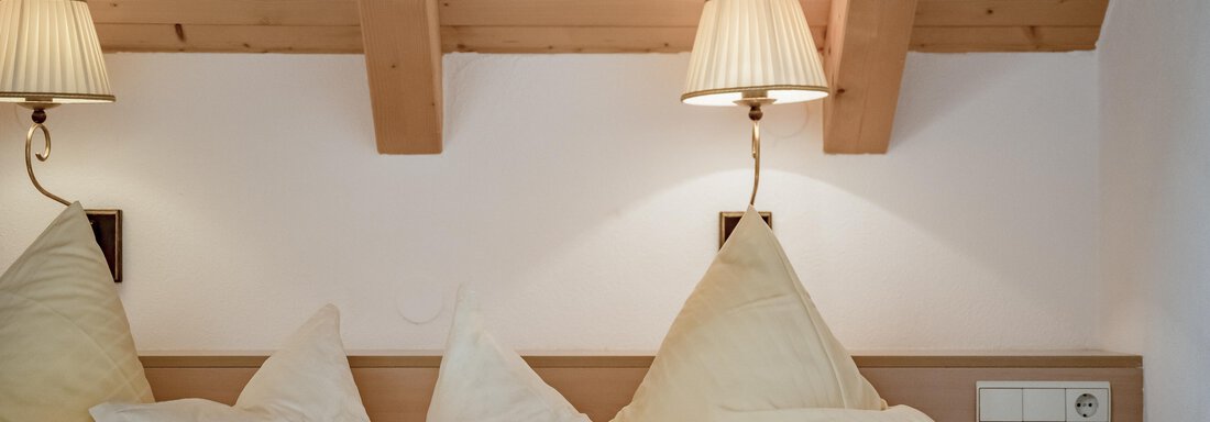 A cozy bedroom with a wooden ceiling and soft lighting. The beds are equipped with large, white pillows. - Villa Castelbell - Sölden