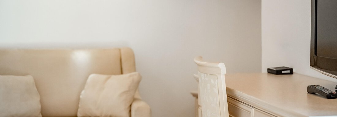A cozy living room with a beige sofa and a desk. A television is mounted on the wall. - Villa Castelbell - Sölden