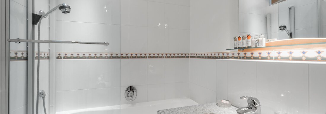 A modern bathroom with a bathtub and a shower partition. The sink area is equipped with an elegant mirror and decorative accessories. - Villa Castelbell - Sölden
