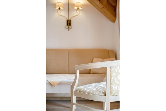 A cozy living room with a beige sofa and a white chair. The walls are light, and two wall lamps provide soft light. - Villa Castelbell - Sölden